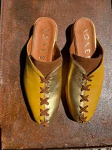 Zapatos chatos color dorado y mostaza con cordones decorativos.