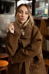 Campera de efecto gamuza color tostado con interior de corderito sintético. Presenta cierre frontal, bolsillos delanteros con solapa, cintura ajustable con cordón y puños con detalle de corderito.