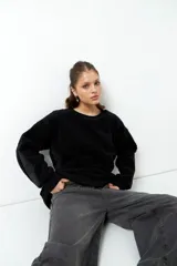 Buzo negro de tela tipo teddy, de manga larga y cuello redondo. Presenta recortes de nylon en mangas y laterales.