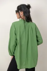 Camisa de algodón verde con bordados al tono, escote en V y cuello camisero corto, mangas tres cuartos abullonadas con puños elásticos y cierre frontal parcial con botones.