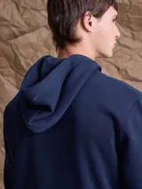 Canguro con cierre frontal completo, confeccionado en tejido fleece de color azul marino. Presenta capucha con cordones ajustables, bolsillos laterales y puños y ruedo acanalados.