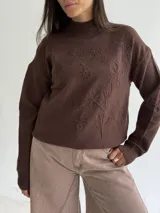 Sweater de punto color blanco con cuello polera, manga larga y diseño bordado al tono con motivos florales en el frente y las mangas.