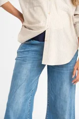 Jean de maternidad con corte wide leg y tiro medio, confeccionado en denim de algodón con acabado deshilachado en el ruedo.