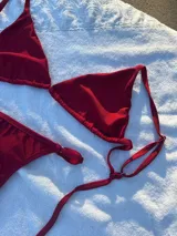 Conjunto de bikini rojo brillante, compuesto por un corpiño triangular con tirantes finos y una tanga con tirantes laterales ajustables.