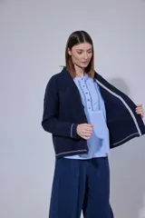 Saco tejido en lambswool con diseño de rombos y trenzas en el frente. Presenta cierre frontal con botones, cuello en V y detalles de rayas en contratono en puños y ruedo. Incluye pin bordado en la manga.