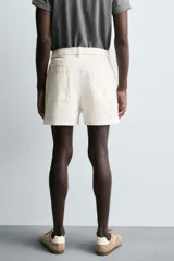Shorts de algodón color blanco roto, de corte regular fit, con cintura ajustable mediante cinturón del mismo tejido y hebilla metálica. Presenta bolsillos delanteros y bolsillos traseros de vivo.