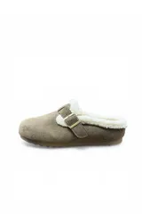 Zueco de gamuza color caqui con forro y reborde de corderito sintético blanco, tira con hebilla metálica ajustable en el empeine y suela plana.