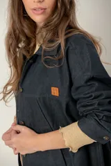 Campera de jean oversize color negro, con corte largo, cuello camisero, cierre frontal con botones metálicos y bolsillos frontales. Presenta un parche de cuero con logo en el pecho.