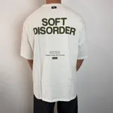 Remera de corte oversize color blanco con estampado gráfico en la espalda en color verde oliva que incluye el texto 'SOFT DISORDER' y detalles de marca.