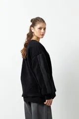 Buzo negro de tela tipo teddy, de manga larga y cuello redondo. Presenta recortes de nylon en mangas y laterales.