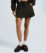 Short pollera de gamuza sintética color verde oliva, con diseño de tablas en el ruedo, cintura con trabillas y bolsillos delanteros.