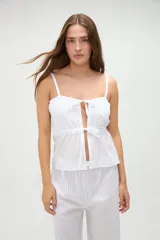 Top de pijama blanco confeccionado en algodón, con tirantes finos, escote recto y aberturas frontales con lazos ajustables.