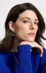 Caravana de diseño orgánico con acabado dorado y piedra central en tono verde intenso. Presenta una forma rectangular de bordes suaves y cierre de pasador.