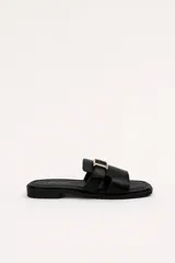 Sandalias planas Daniel Cassin modelo Floren, color negro, con tira ancha en el empeine decorada con una hebilla metálica dorada y diseño de punta cuadrada.