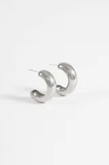 Aros tipo argolla de diseño grueso y acabado pulido brillante, fabricados en acero quirúrgico hipoalergénico.