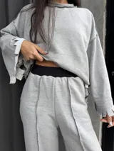 Buzo oversize de color gris, con diseño de costuras expuestas en contraste y terminaciones desflecadas en mangas y ruedo.