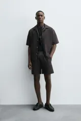 Bermuda de hombre, corte regular fit, color oscuro con patrón de rayas verticales finas en tono marrón claro. Presenta cintura elástica ajustable con cordón interior, bolsillos frontales y un bolsillo trasero de plastrón.