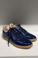 Championes de cuero vacuno con acabado brillante tipo charol, color azul marino, con cordones al tono y suela de goma color caramelo.