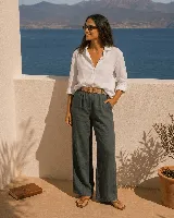 Pantalón de lino color verde oscuro, de corte ancho y relajado, con cintura elástica y cinto de rafia con hebilla redonda.