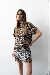 Blusa de seda con estampado floral en tonos beige y negro, cuello alto, manga japonesa y detalle de botones laterales.