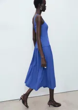 Vestido midi de color azul, sin mangas, con tirantes anchos y cuello escotado cuadrado. Presenta un diseño ajustado en el torso con corte evase y falda de corte midi con vuelo.