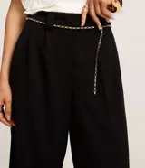 Pantalón wide leg de crepé color blanco, con trabillas en la cintura, cierre tradicional, pliegues frontales y detalle de cinturón de cadena.