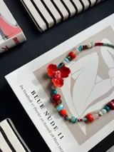 Collar corto de abalorios multicolor con cuentas de diferentes formas, tamaños y materiales, destacando un gran dije central en forma de flor roja.