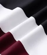 Campera con capucha de estilo deportivo, confeccionada en poliéster con diseño de paneles en colores negro, blanco y bordó. Presenta cierre frontal con cremallera, puños elásticos y bolsillos laterales.