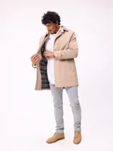 Gabardina de corte clásico en color beige, con cierre frontal de cremallera y botones, cuello camisero y puños ajustables con trabillas.
