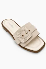 Sandalias planas de color beige claro con capellada ancha y hebilla cuadrada decorativa forrada en material trenzado.