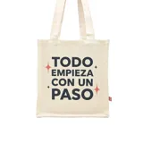 Tote bag de tela color beige con estampado frontal en color negro y detalles de estrellas en rojo y negro. Cuenta con dos asas largas para llevar al hombro.