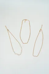 Set de tres collares dorados de diferentes diseños: uno con corazones y perlas, otro de eslabones y el último de cadena fina.