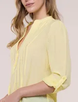 Blusa de gasa bambúla color amarillo, marca Zac & Rachel, con cuello a la base y escote en V con botones frontales. Presenta diseño delantero plisado y mangas largas con sistema de ajuste mediante presilla.
