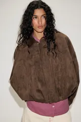 Chaqueta de efecto ante color marrón claro, con cuello solapa, manga larga con trabillas en los hombros y bajo abullonado. Cierre frontal con cremallera y botones ocultos por solapa.