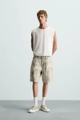 Bermuda relaxed fit confeccionada en tejido de algodón con efecto lavado. Presenta un diseño de cinco bolsillos, bolsillo multifunción en la pernera y tira lateral de estilo carpintero. Cuenta con cierre frontal con cremallera y botón.