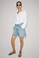 Shorts denim de tiro alto y corte relaxed, confeccionados en tejido vaquero celeste claro. Presentan trabillas en la cintura, diseño de cinco bolsillos, pliegues frontales y cierre con cremallera y botón metálico.