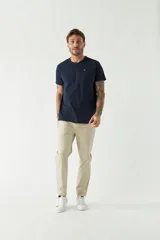 Pantalón chino color beige, corte slim, con bolsillos laterales y traseros. Se ajusta a la cintura con cinturón de cuero marrón.