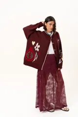 Saco de punto color vino con diseño holgado, cuello redondo y mangas largas. Presenta un gran bordado central en la espalda con forma de flor en tonos crema y rojo, acompañado de un pequeño bordado de sol y una frase bordada en la parte inferior.