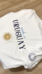 Remera de algodón premium color crema, con corte holgado y cuello redondo. Presenta un bordado en el pecho con diseño de estampilla que incluye un sol, un mate y un caballo, además de un bordado de herradura en la manga derecha.