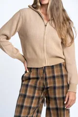 Campera tejida de algodón con cierre frontal completo y cuello alto. Presenta una textura acanalada vertical y puños y ruedo elásticos.