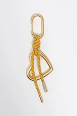 Llavero con mosquetón metálico dorado, cordón trenzado amarillo y marrón con detalles blancos, y dije en forma de corazón.