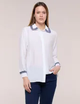 Camisa de crepe liviana y texturada color blanco, de silueta relajada y holgada, con cuello camisero clásico y puños con detalles de bordado de pasamanería con terminación deshilachada y aplique de perlas. Cuenta con cartera de botones oculta al frente y mangas largas.