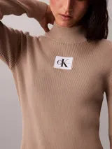 Vestido mini de Calvin Klein color beige, confeccionado en tejido de punto acanalado con cuello alto, manga larga y ajuste ceñido al cuerpo. Cuenta con una etiqueta con el logo de la marca en el pecho.
