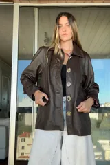 Tapado de cuero ovino color chocolate con detalles de pasamanería y presillas en gamuza al tono. Presenta cierre frontal con botones grandes y mangas largas con puños ajustados.