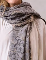 Bufandón de tejido suave con estampado de arabescos en tonos grises y beige, con terminación de flecos en los extremos.