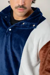 Buzo de textura afelpada con diseño de bloques de color en azul, blanco y marrón. Presenta cuello alto con cierre frontal parcial mediante botones a presión.