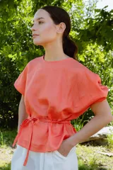 Blusa color salmón de manga tres cuartos con leve volumen, largo hasta la cadera y cinto extraíble en la espalda.