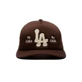 Gorro trucker marrón con diseño de red en la parte trasera, visera curva y bordado frontal en relieve color beige con letras "LA" y el texto "Mi Casa Su Casa".