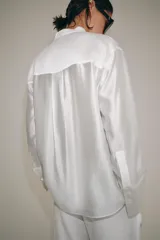 Camisa de cuello redondo y manga larga con puños anchos. Presenta un bolsillo de plastrón en el pecho con detalles de bordados a tono, los cuales también se encuentran en los puños. Cierre frontal con botones ocultos por tapeta.