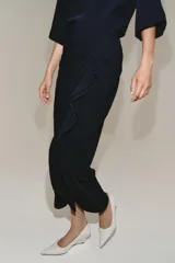 Vestido midi de cuello redondo y manga corta, confeccionado en tejido fluido color azul marino. Presenta un diseño con detalle de drapeado y volado lateral en la parte delantera, con cierre en la espalda mediante abertura y botón.
